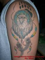 Tatuaje de un collar indio, con plumas y colmillos, con una cabeza de águila y una huella detrás