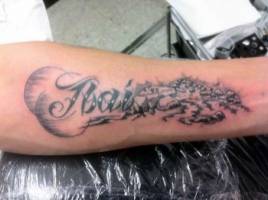 Tatuaje de un nombre en el antebrazo con un paisaje de rio