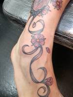 Tatuaje de una flor con lazos y pétalos en color en la pierna y pie 