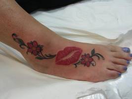 Tatuaje de unos labios y unas flores a color en el pie