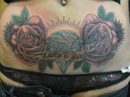 Tatuaje a color de dos rosas y un diamante con una frase en la barriga de una chica