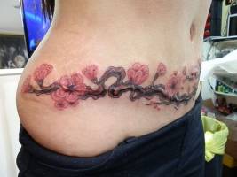 Tatuaje de una rama con flores en la barriga y cintura de una chica