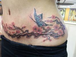 Tatuaje de una rama de árbol a color con flores y una mariposa