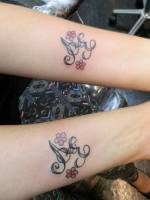 Tatuaje  de dos letras con flores en cada antebrazo