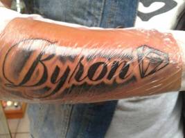 Tatuaje en el antebrazo del nombre Byron con un diamante