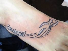 Tatuaje de un nombre con unas plantas y estrellas en el pie