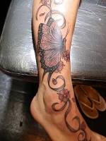 Tatuaje a color de una gran mariposa en el tobillo con una cinta  y flores