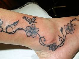 Tatuaje de una planta con flores y una mariposa a color