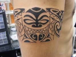 Tatuaje de un brazalete tribal con mascara maorí