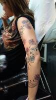 Tatuaje de una planta con flores enrollada al brazo de una chica