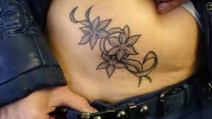 Tattoo de una planta con flores en la cintura
