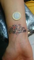 Pequeño tattoo de la frase One love con pétalos y una flor