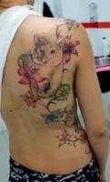 Tatuaje de un gato y una enredadera con flores en la espalda de una chica