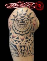 Tatuaje blanco y negro de una mascara maorí en el hombro y brazo