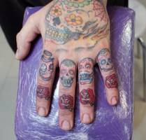 Tatuajes de calaveras mexicanas y rosas en la mano y cada uno de los dedos