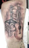 Tatuaje de una guitarra española y una silla
