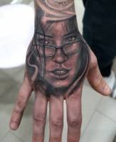 Tatuaje en la mano de una cara de chica con gafas 