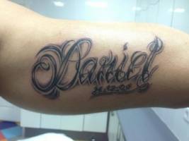 Tatuaje de un nombre con una fecha debajo en el brazo