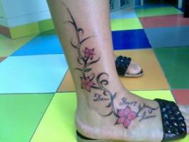 Tattoo de una enredadera en el pie de una chica con flores y nombres