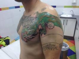 Tatuaje de un dragón con algunas flores del brazo al pecho