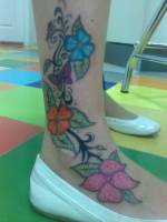Enredadera con flores y mariposas tatuadas en el tobillo de una chica