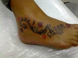 Tatuaje del nombre Mirna en el pie, con decoración de plantas y flores
