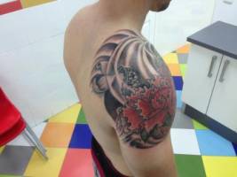 Tatuaje de una flor con una carpa debajo en el hombro de un chico