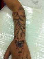 Tatuaje de una planta en el antebrazo con una mariposa en la mano