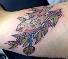 Tatuaje de un pájaro en una rama con frutos y un colgante