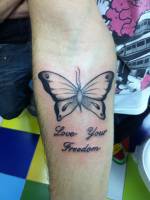 Tatuaje de una mariposa en el antebrazo con una frase