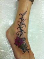 Tatuaje de una planta con hojas, flores y una mariposa tatuadas en el tobillo