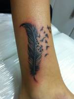 Tatuaje de una pluma separándose en miles de pájaros