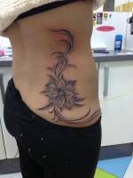 Espalda de chica tatuada con una flor con sus hojas