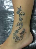 Tobillo tatuado con una enredadera con flores y mariposas