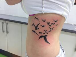 Pájaros volando tatuados en las costillas de una chica