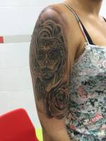 Tatuaje de una calavera mexicana con una rosa en el brazo de una mujer