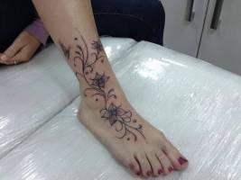 Enredadera con flores tatuada en el pie