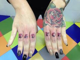 Tatuaje de una rosa en la mano, y las palabras DAD y MOM en los dedos