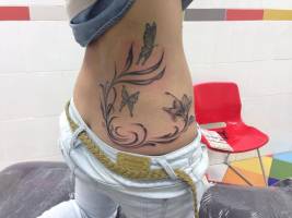 Tatuaje de unas plantas, flores y mariposas en la espalda de una chica