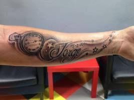 Tatuaje de un reloj, estrellas y un nombre