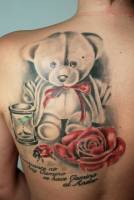Tatuaje de un oso de peluche, un reloj de arena, una rosa y una mariquita junto con una frase
