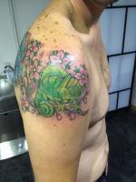 Tattoo a color de un camaleón en una rama con flores