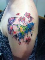 Tatuaje de un colibri con flores, con manchas de pintura