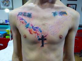 Tatuaje de una cruz en el pecho con manchas de pintura