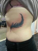 Tatuaje de una pluma a color en el costado de una chica