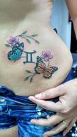 Tatuaje de un par de mariposas y flores, junto a un símbolo del horóscopo