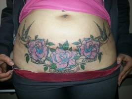 Tatuaje de tres grandes rosas y un par de golondrinas debajo de la barriga de una mujer