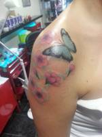 Tatuaje de una mariposa y flores en el hombro de una mujer