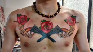 Tattoo de pistolas cruzadas en el pecho, y cintas con una frase