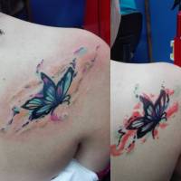 Tattoo de una mariposa con manchas de pintura en la espalda de una chica
